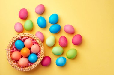 Sarı arka planda renkli Paskalya yumurtaları olan dekoratif bir yuva.