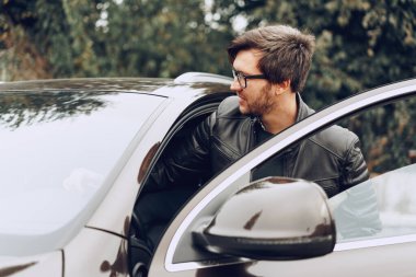 Gözlüklü şık bir adam arabada oturuyor.