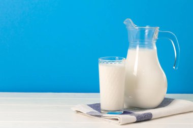 Mavi arka plana karşı bardak ve sürahi süt