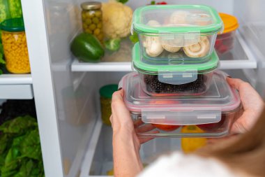 Kadın eli buzdolabından yiyecek dolu bir kutu alıyor.