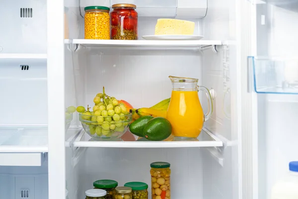 Glaskanne mit Orangensaft und Früchten im Kühlregal — Stockfoto