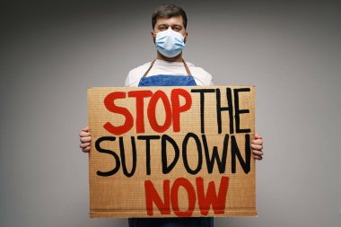 Erkek protestocu, gri arkaplana karşı koronavirüs kilitlerine karşı pankart tutuyor