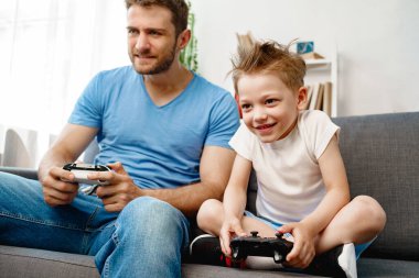 Babası ve küçük oğlu evde video oyunu oynuyorlar.