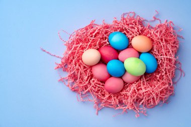 Mavi arka planda dekoratif yuvada renkli Paskalya yumurtaları