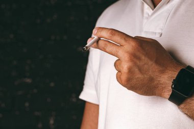 Siyah arka planda yanan sigarayı tutan erkek el.