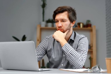 Genç adam çalışma masasında dizüstü bilgisayarla çalışıyor.