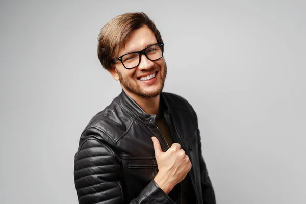 Portrait of a young man in glasses wearing black leather jacket on grey background — Stock Photo, Image