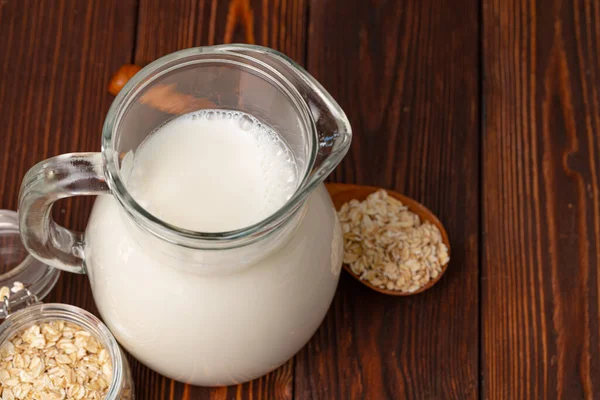 Jarra de vidrio de leche y copos de avena sobre mesa de madera —  Fotos de Stock