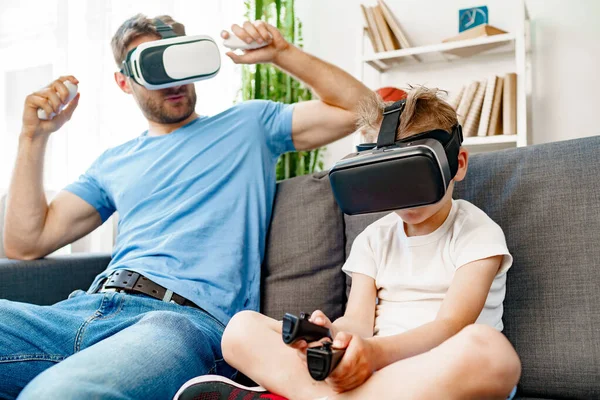 Baba oğul kanepede oturup VR gözlükleriyle oyun oynuyorlar.