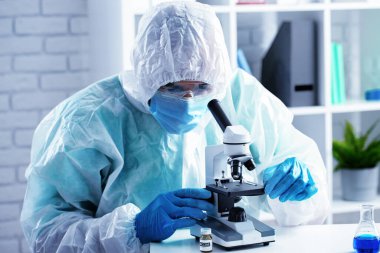 Mikroskop altında koruyucu elbise giyen bir tıp çalışanı.