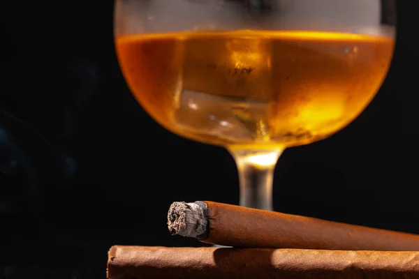 Verre de whisky et cigare allumé sur fond noir — Photo