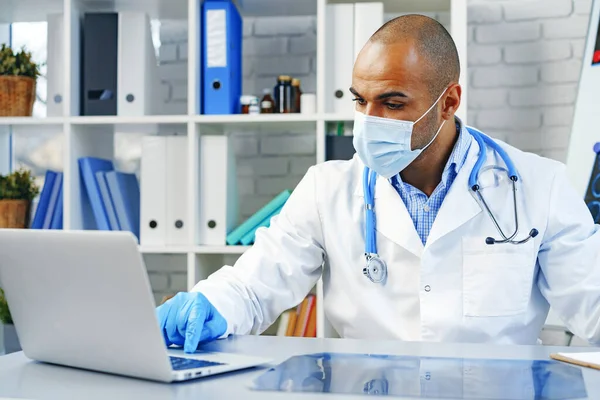Karışık ırk erkek doktoru hastanede çalışma masasında oturuyor. — Stok fotoğraf