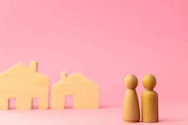 Ahşap ev minyatürü ve pembe arka planda oyuncak insanlar.