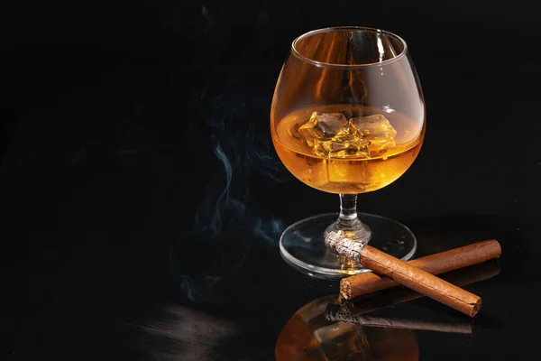 Verre de whisky et cigare allumé sur fond noir — Photo