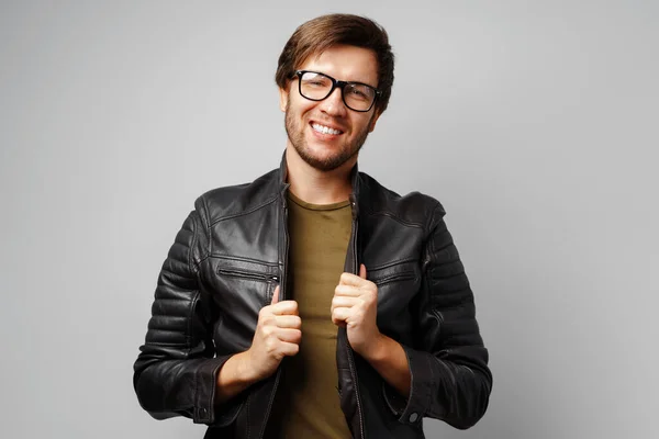 Portrait of a young man in glasses wearing black leather jacket on grey background — Stock Photo, Image