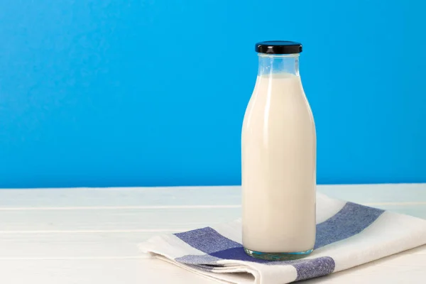 Glass bottle of milk on wooden table against blue background — Stock Photo, Image