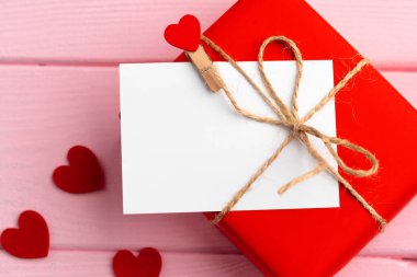 Kırmızı hediye kutusu ve pembe arka planda tebrik kartı.