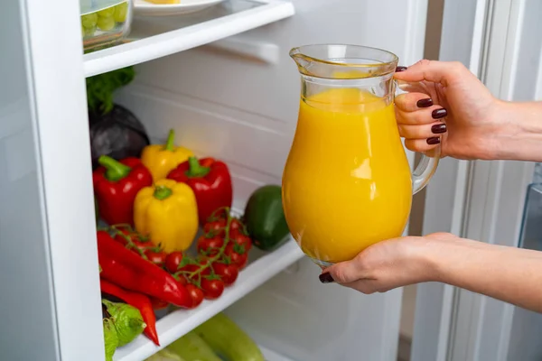 Vrouwelijke hand neemt sinaasappelsap pot uit een koelkast — Stockfoto