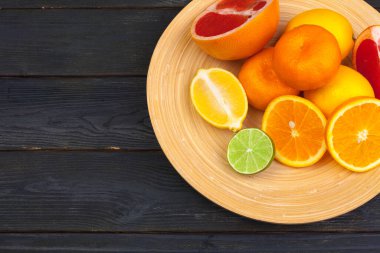 Siyah ahşap arka planda bir kase turunçgil meyvesi.