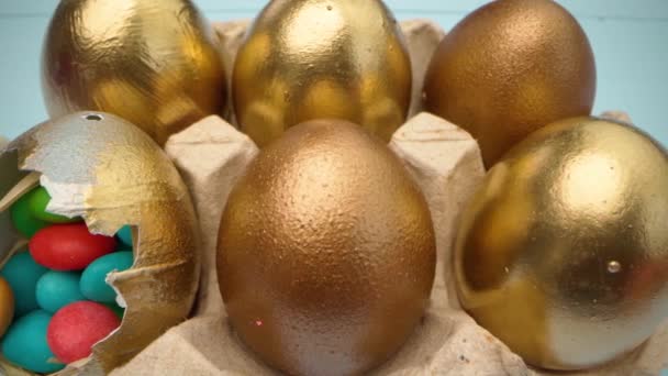 Золоті декоративні великодні яйця, наповнені барвистими цукерками на дерев'яному столі крупним планом — стокове відео