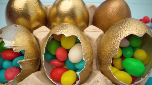 Oeufs de Pâques décoratifs dorés remplis de bonbons colorés sur une table en bois close up — Video