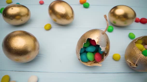Χρυσά διακοσμητικά πασχαλινά αυγά γεμάτα με πολύχρωμες καραμέλες σε ξύλινο τραπέζι από κοντά — Αρχείο Βίντεο