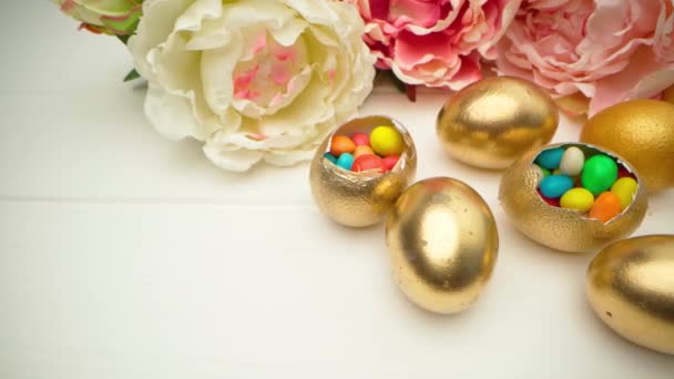 Altın dekoratif Paskalya yumurtaları ahşap masada renkli şekerlemelerle dolu. — Stok video