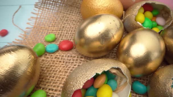 Gyllene dekorativa påskägg fyllda med färgglada godis på träbord på nära håll — Stockvideo