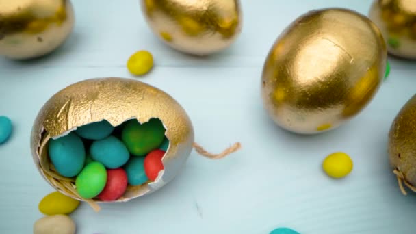 Χρυσά διακοσμητικά πασχαλινά αυγά γεμάτα με πολύχρωμες καραμέλες σε ξύλινο τραπέζι από κοντά — Αρχείο Βίντεο