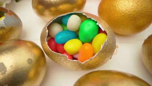 Ovos de Páscoa decorativos dourados cheios de doces coloridos na mesa de madeira close-up — Vídeo de Stock