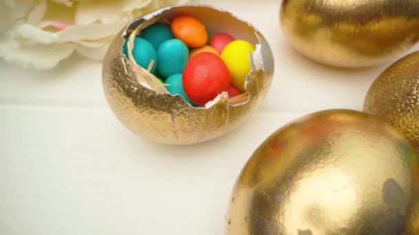 Oeufs de Pâques décoratifs dorés remplis de bonbons colorés sur une table en bois close up — Video