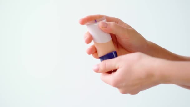 Female hand holding tube with face foundation against white background — Stock Video