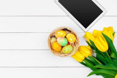 mesaj için tablet ekranı ve renkli laleler ve ahşap zemin üzerinde paskalya yumurtaları