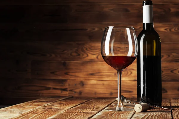 Glass and bottle with delicious red wine on table against wooden background — Stock Photo, Image