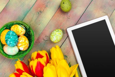 mesaj için tablet ekranı ve renkli laleler ve ahşap zemin üzerinde paskalya yumurtaları