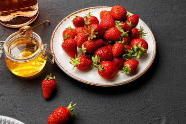 Taze çilekli tabak ve siyah arka planda bir bardak şarap.