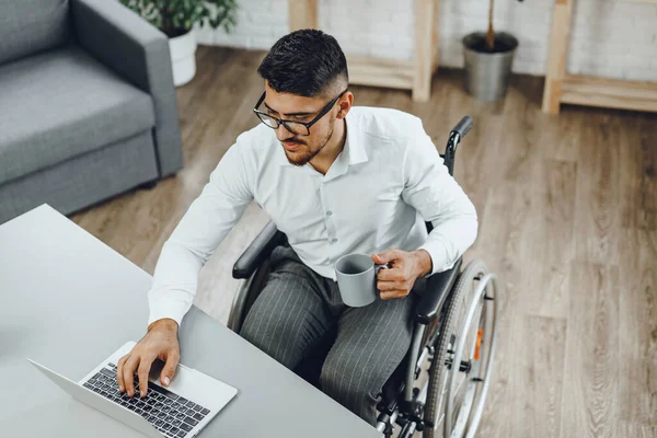 Joven discapacitado positivo en silla de ruedas trabajando en la oficina — Foto de Stock