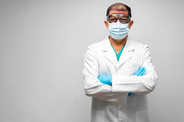 Starszy lekarz w masce twarzy stoi na szarym tle — Zdjęcie stockowe