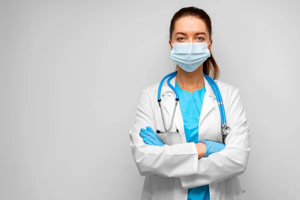 Kobieta lekarz w masce medycznej stoi na szarym tle — Zdjęcie stockowe