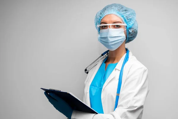 Tıbbi maskeli kadın doktor gri arka planda pano ile ayakta duruyor. — Stok fotoğraf