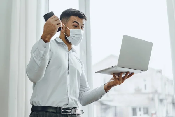 Örömteli üzletember orvosi maszkban tartja laptop és mobil ünnepli a sikert — Stock Fotó