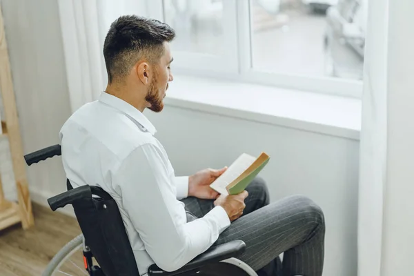 Tekerlekli sandalyedeki engelli adam içeride kitap okuyor. — Stok fotoğraf