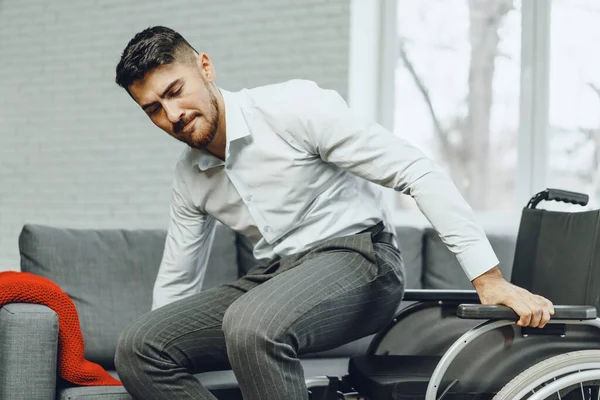 Hombre discapacitado intenta sentarse en un sofá de la silla de ruedas — Foto de Stock