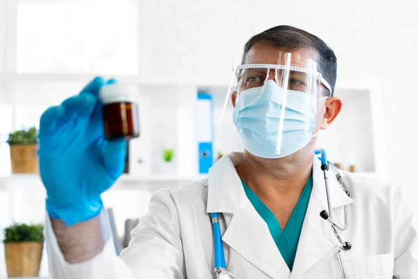 Maskeli kıdemli erkek doktor elinde cam kavanozla ilaç tutuyor. — Stok fotoğraf
