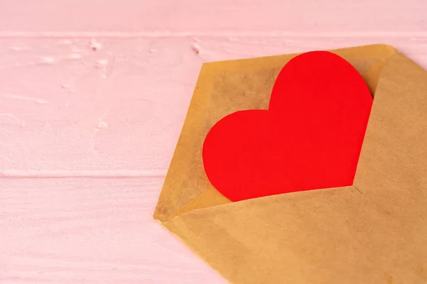 Rote Herzdekoration im Umschlag auf rosa Holztisch — Stockfoto