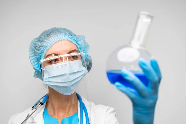 Wissenschaftlerin hält Laborkolben mit chemischer Flüssigkeit, grauer Hintergrund — Stockfoto