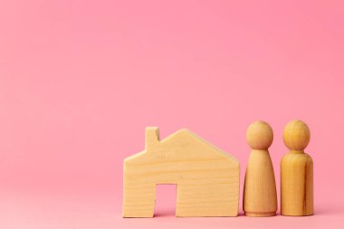 Ahşap ev minyatürü ve pembe arka planda oyuncak insanlar.