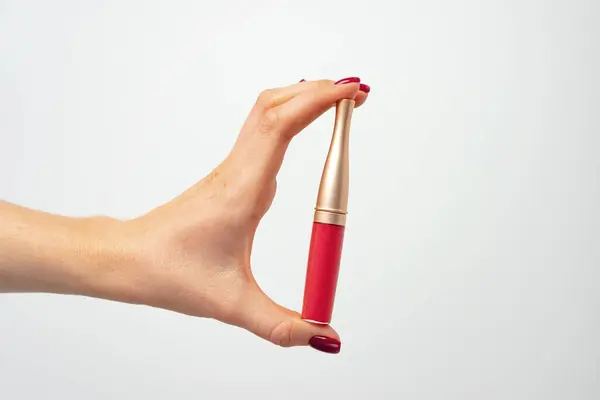 Weibliche Hand hält Lipgloss vor hellgrauem Hintergrund — Stockfoto