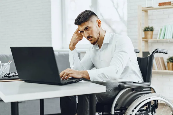 Hombre serio y concentrado en silla de ruedas usando su portátil para trabajar buscando un trabajo en Internet — Foto de Stock