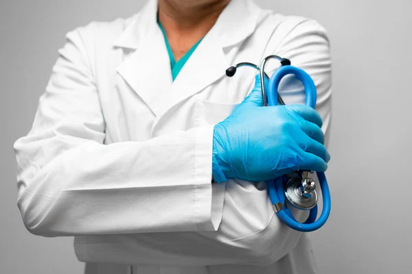 Médico segurando um estetoscópio com os braços cruzados usando luvas azuis — Fotografia de Stock